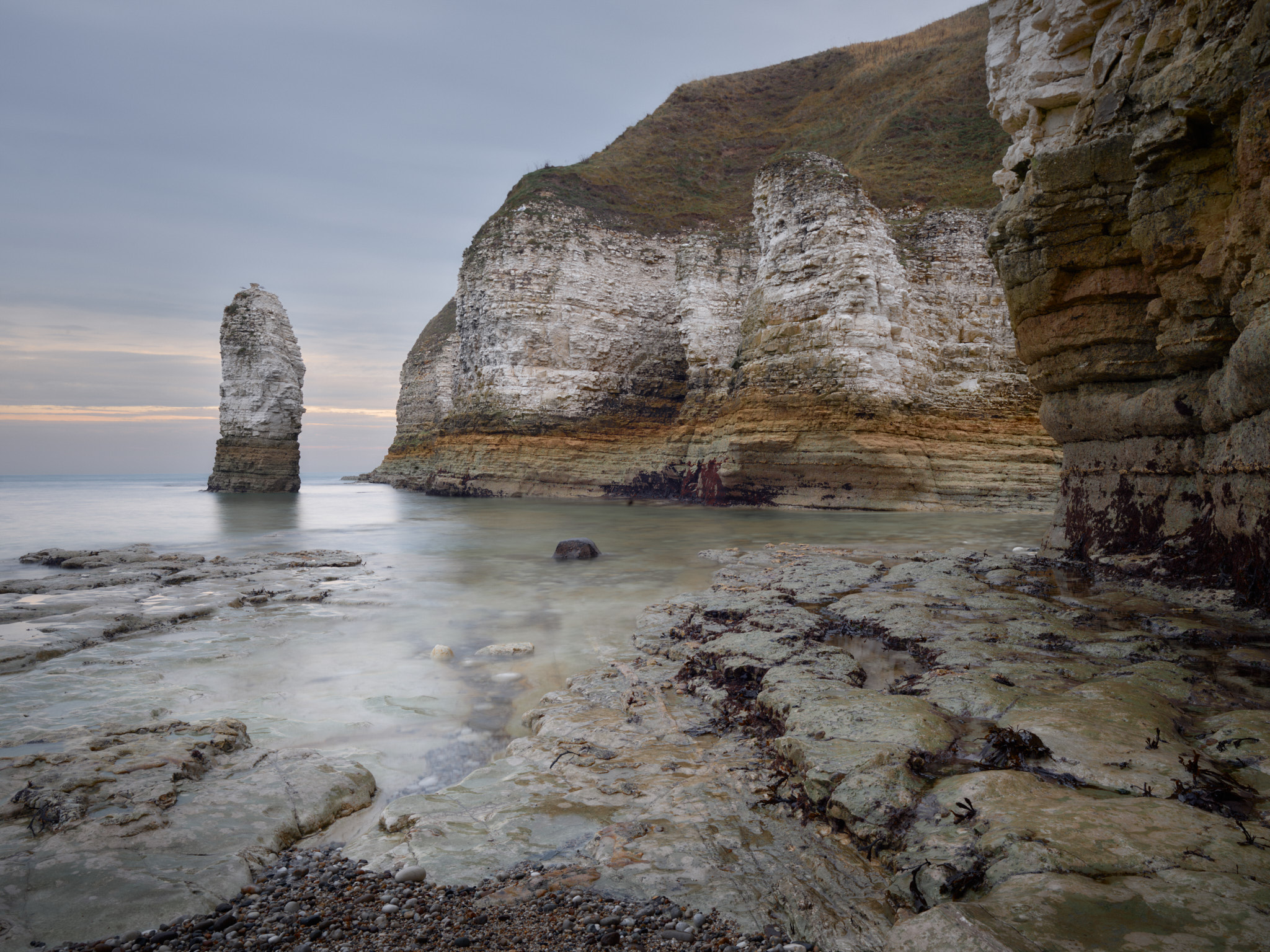 Chalk sea stack and banded white cliffs at Flamborough above a smooth sea, with the wave-cut chalk platform in the foreground as the evening sky starts to colour