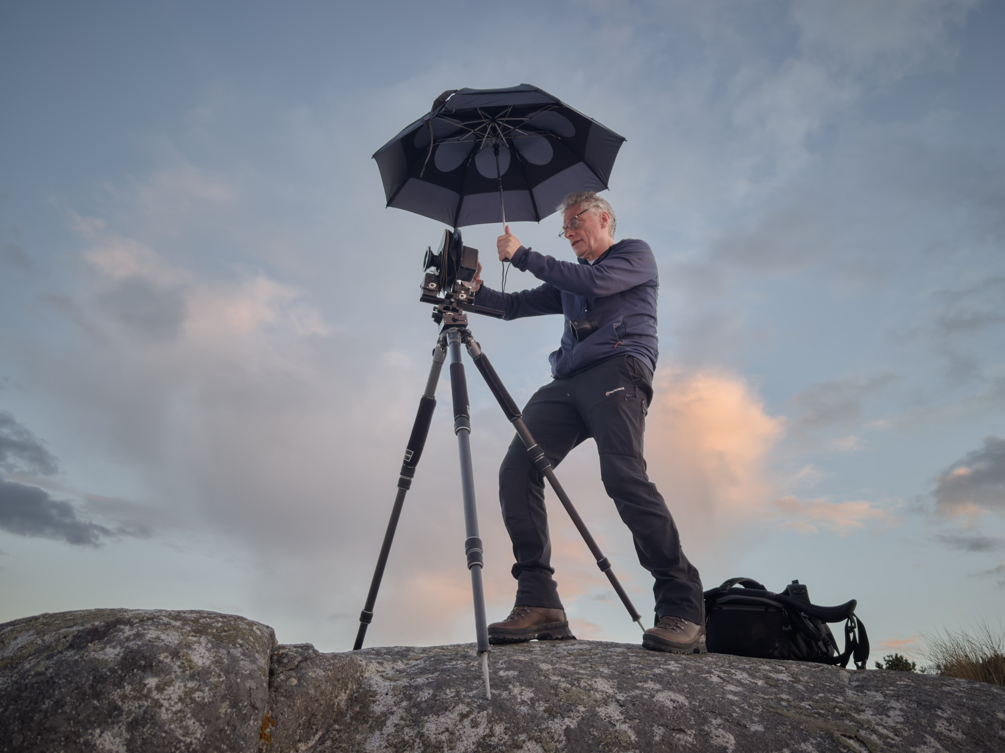Jon Brock in the field with a technical camera and holding an umbrella