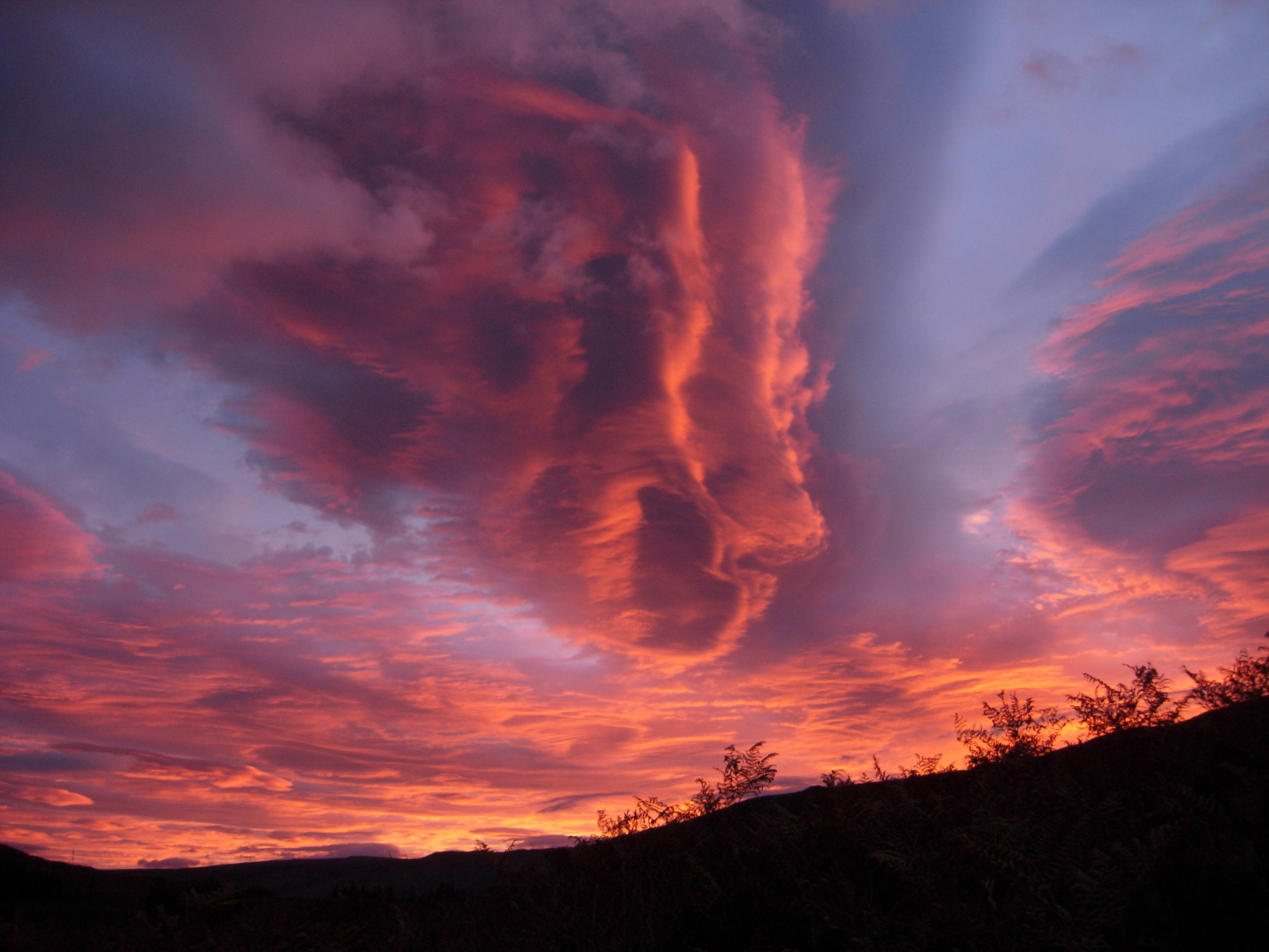 A vast lenticular cloud burning red over the dark moor at dawn