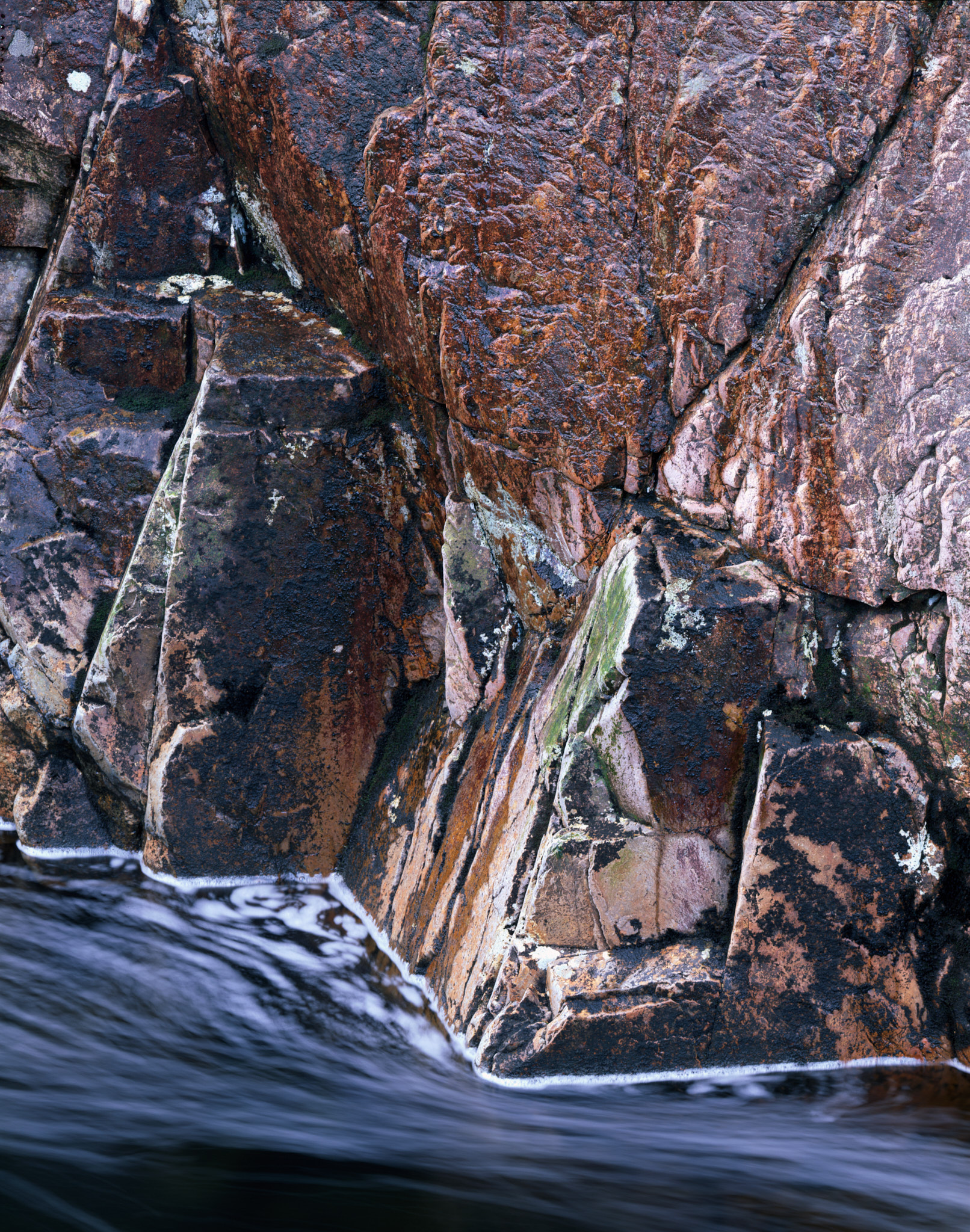 A fractured wall of red and purple rock above the River Etive, white water sliding along its foot