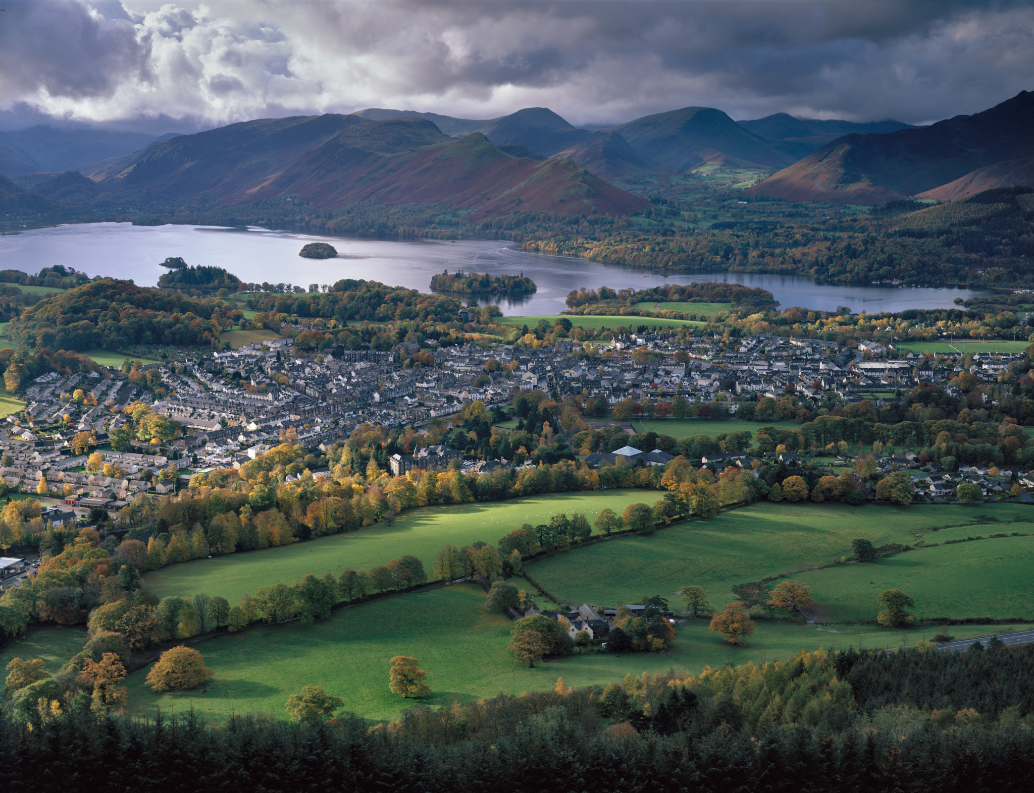 Keswick and Derwent Water from Latrigg, sunlight breaking across the town and fields beneath a dark sky