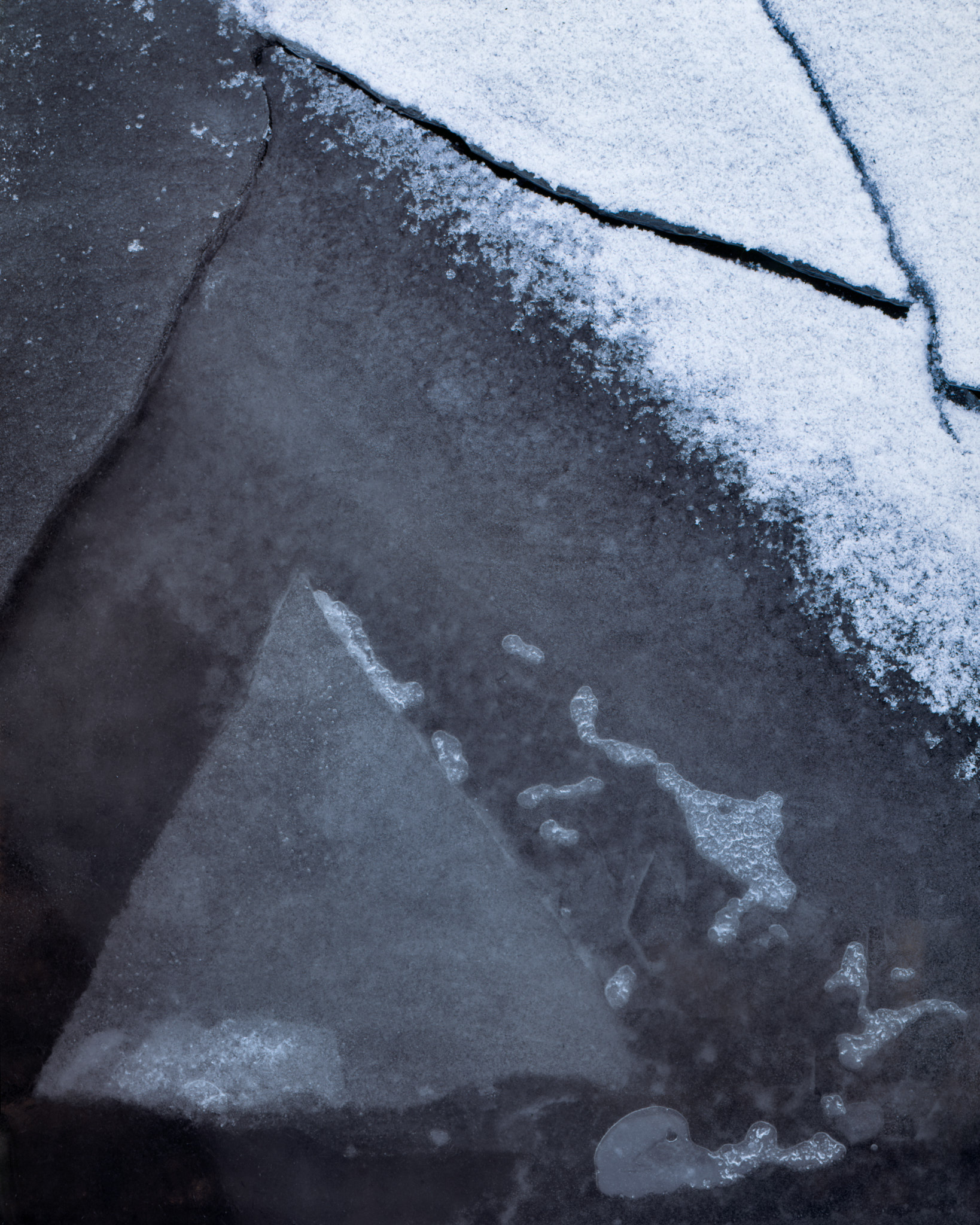 A triangle of pale ice in a frozen puddle on Rannoch Moor, fresh snow along the top edge and lines of ice crossing dark rock