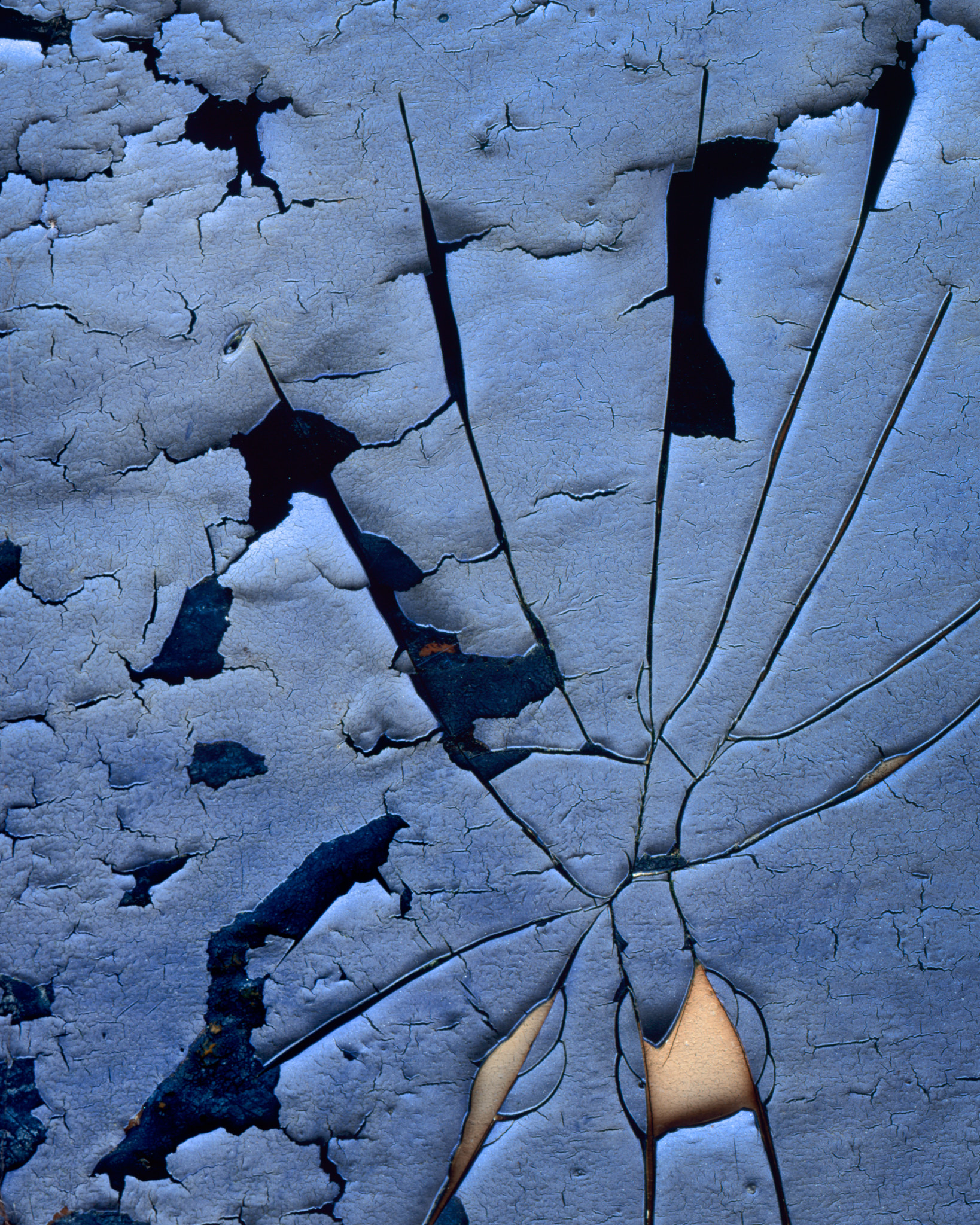 A fan of cracks in weathered blue paint on an upturned boat