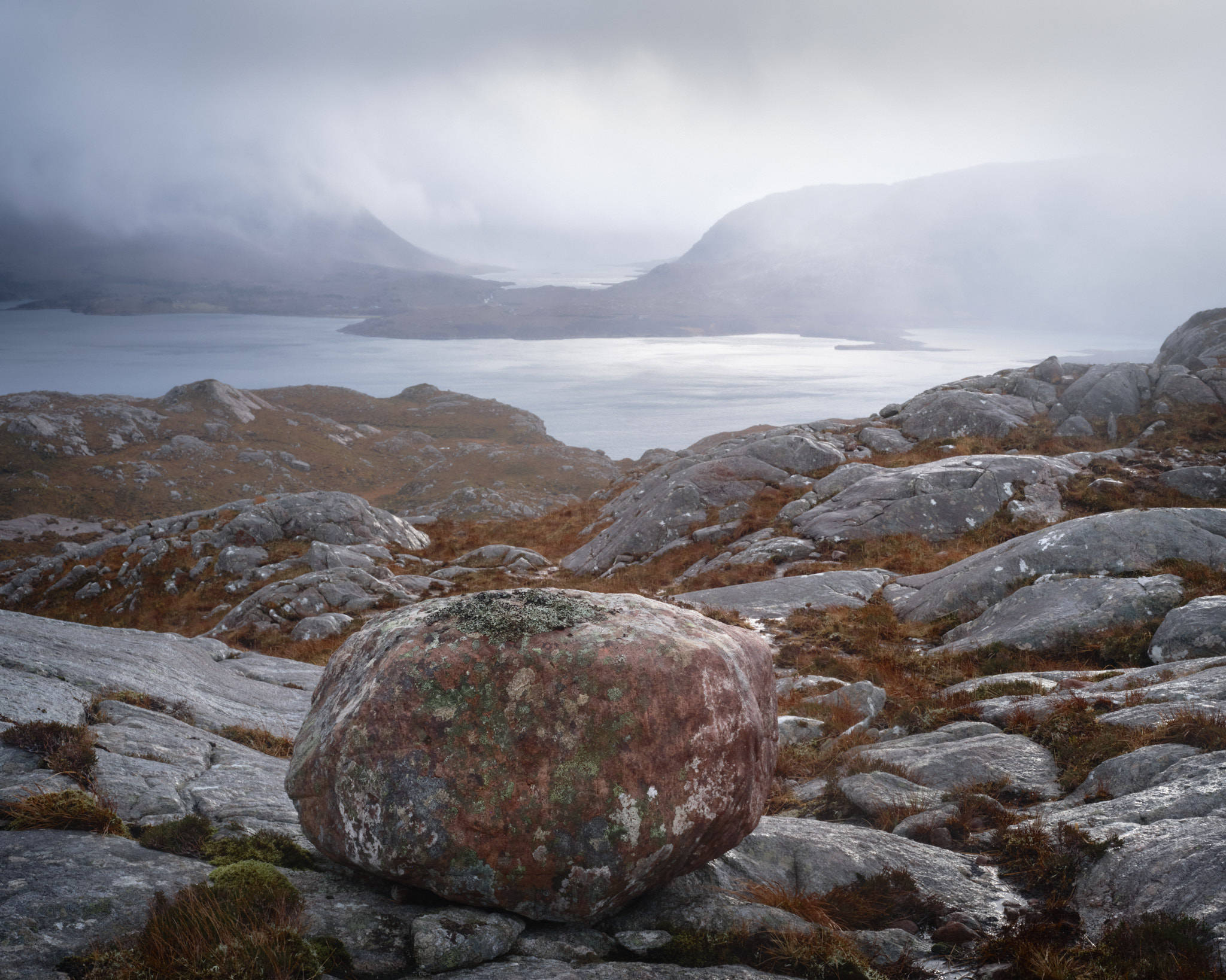 A lichen-covered sandstone boulder on the pass above Torridon, rain sweeping across Upper Loch Torridon below