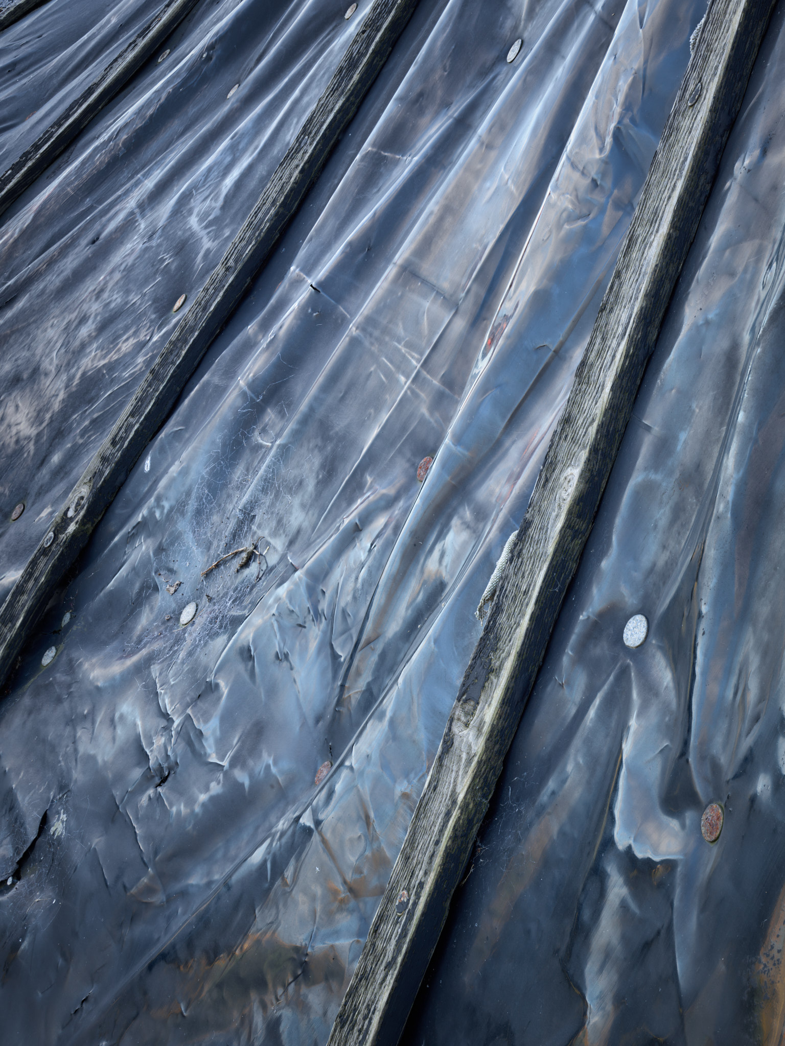 Creased dark membrane over battens on a hut roof, reflecting the sky