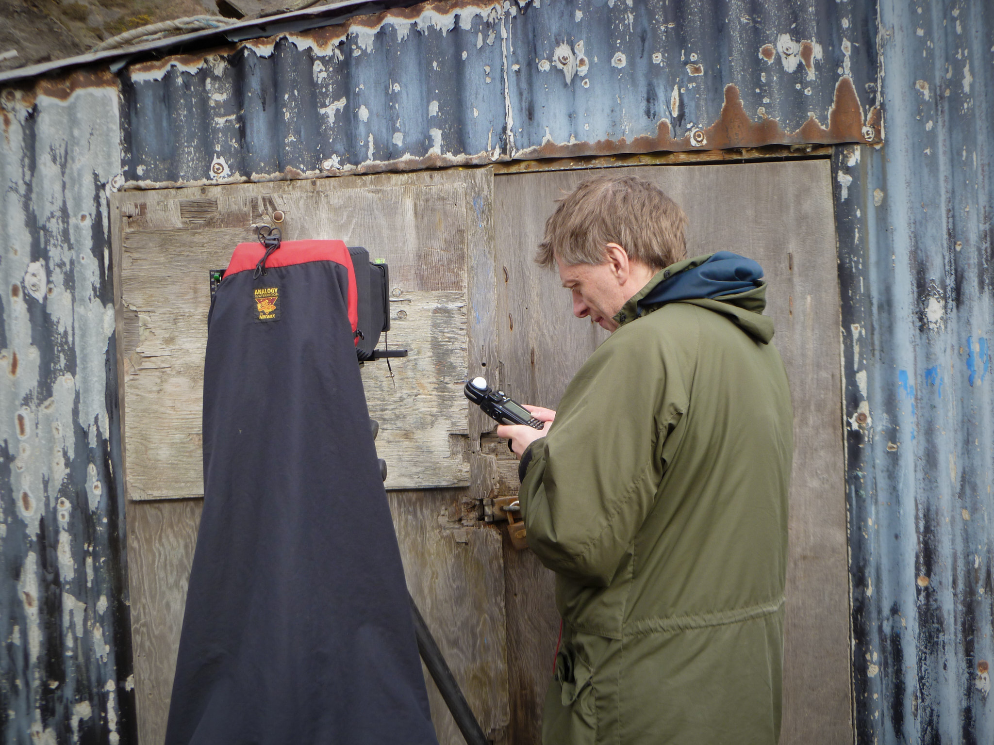 A photographer with a light meter and large-format camera set up on a shed